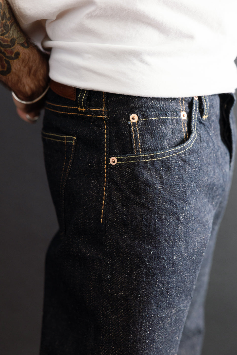 Close-up of the front side of a male model's dark indigo selvedge denim jeans, showing stitching and pocket details.