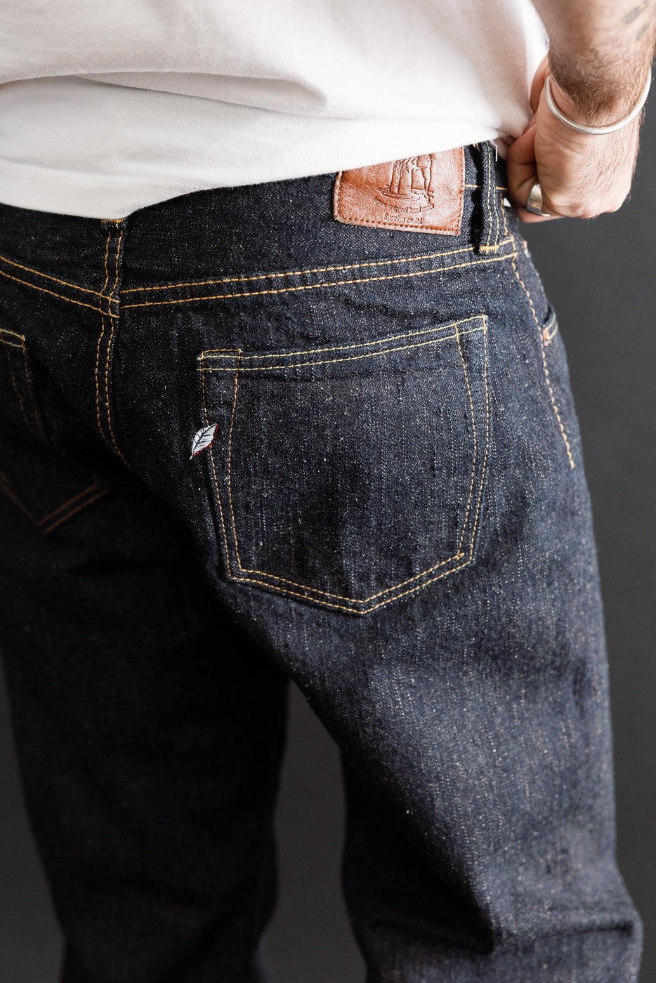 Close-up of the back right pocket and leather patch on dark indigo denim jeans worn by a male model.