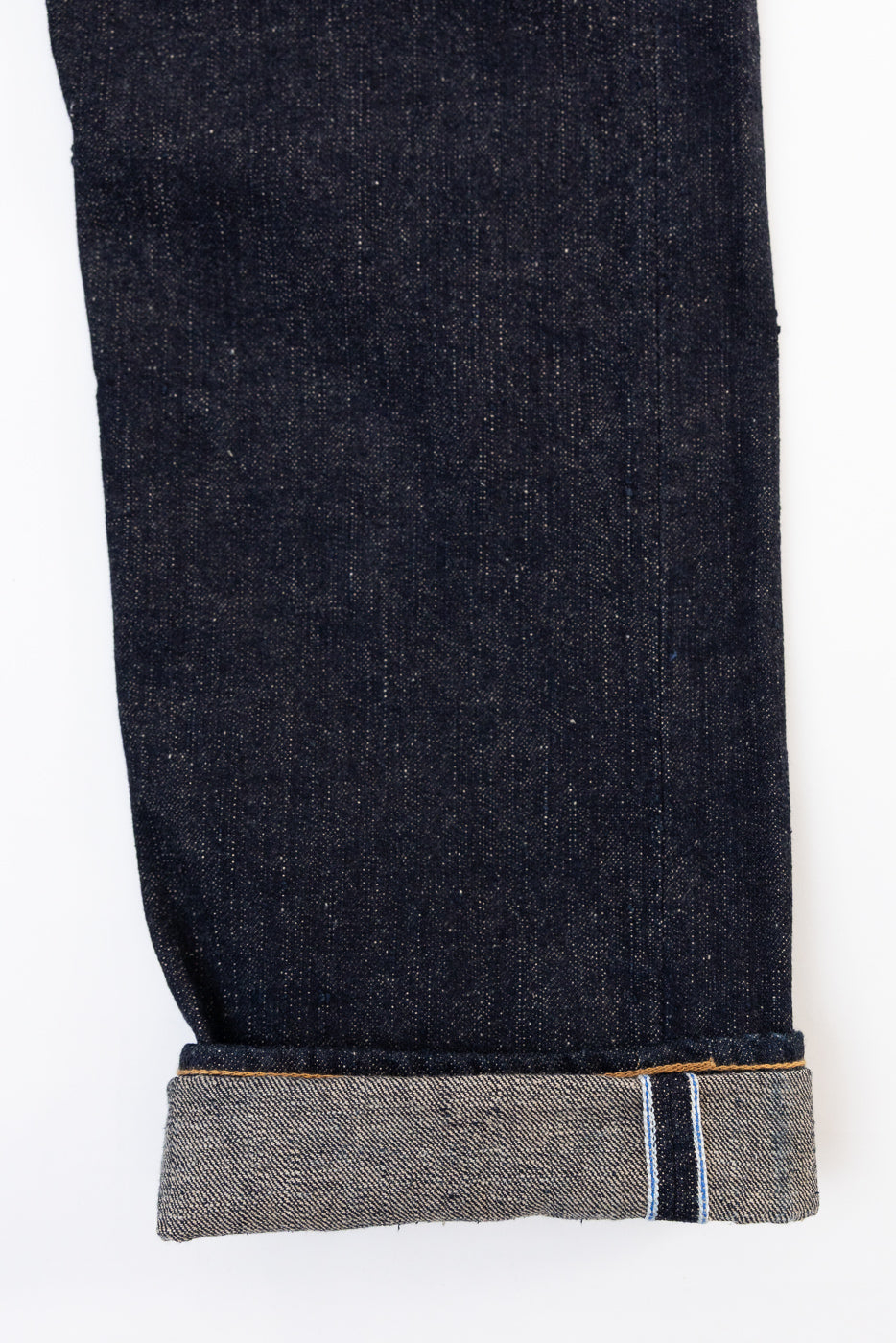 Close-up of the bottom cuff and selvedge detail on the front of dark indigo denim jeans.