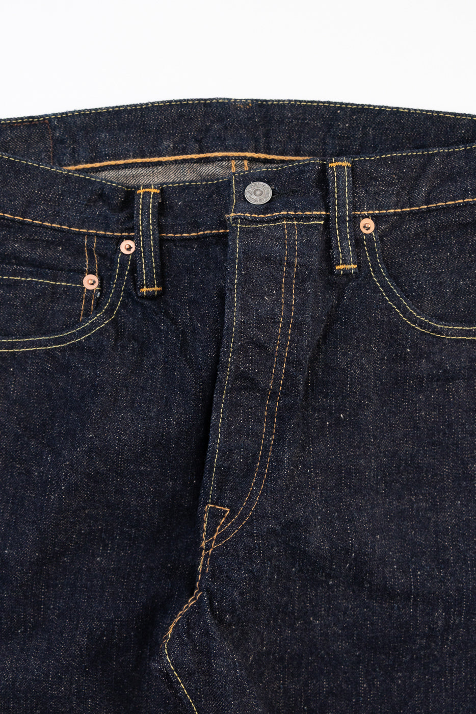 Close-up front view of dark indigo selvedge denim jeans showing button fly and stitching details.