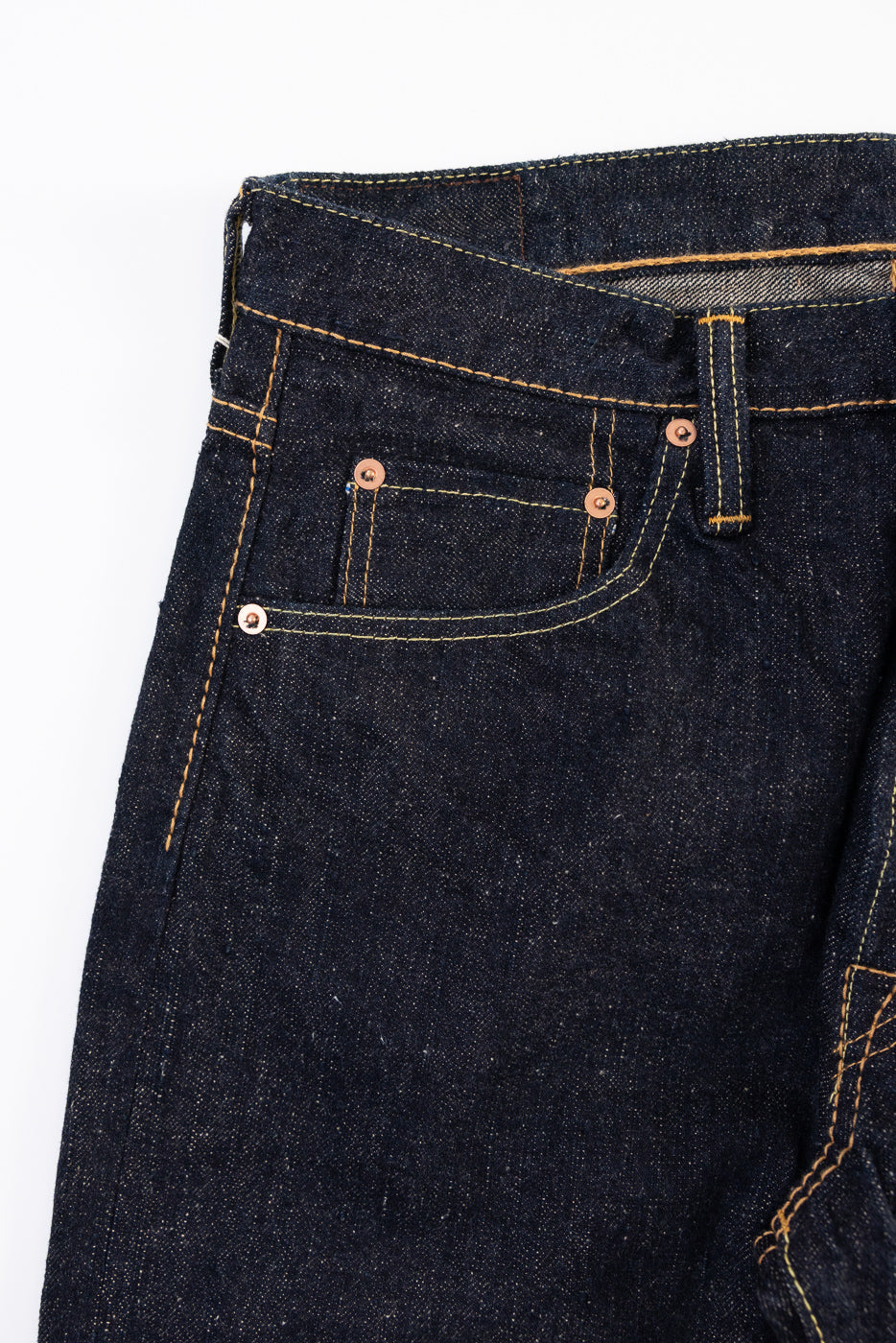 Close-up front view of dark indigo selvedge denim jeans showing pocket stitching and rivets.