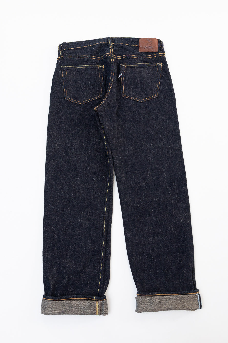 Back view flat lay of dark indigo selvedge denim jeans with rear pockets and leather patch.