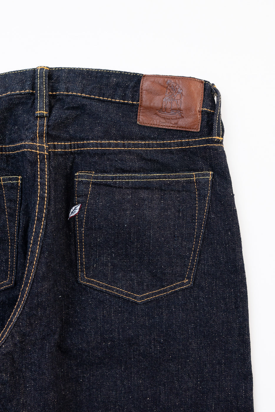 Close-up back view of dark indigo selvedge denim jeans showing the back pocket and leather waistband patch.