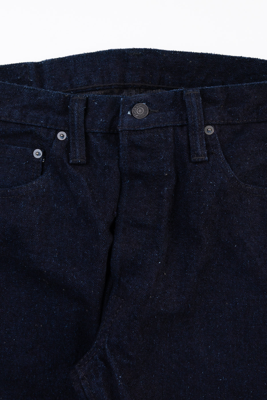 Close-up front view of dark indigo denim waistband, button fly, and metal button detail.