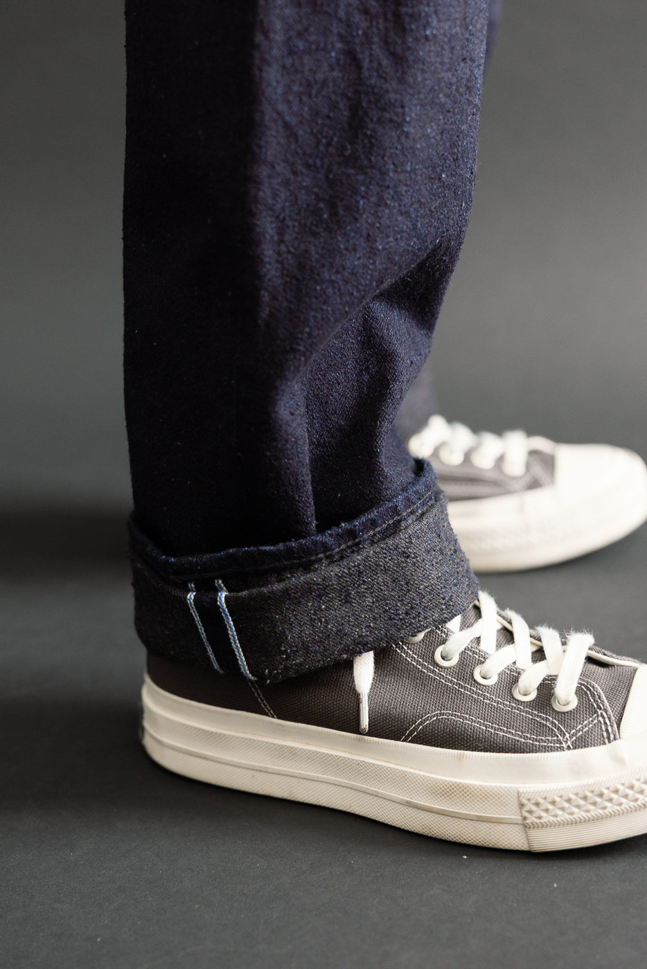 Close-up of the cuffed hem of dark selvedge denim jeans and canvas sneakers on a male model.