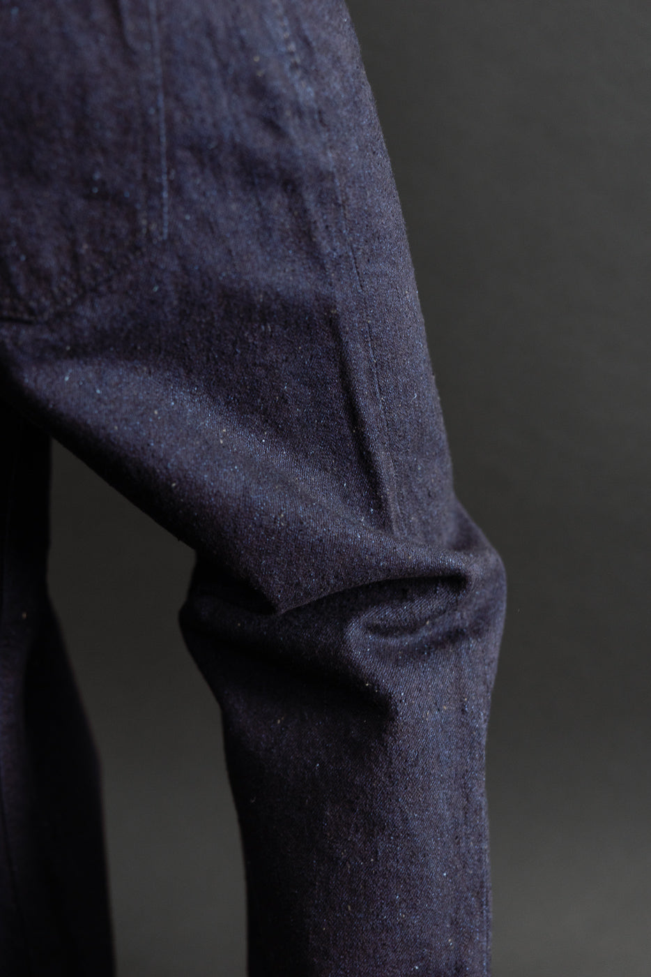 Close-up of the sleeve and side texture of a dark indigo denim garment.