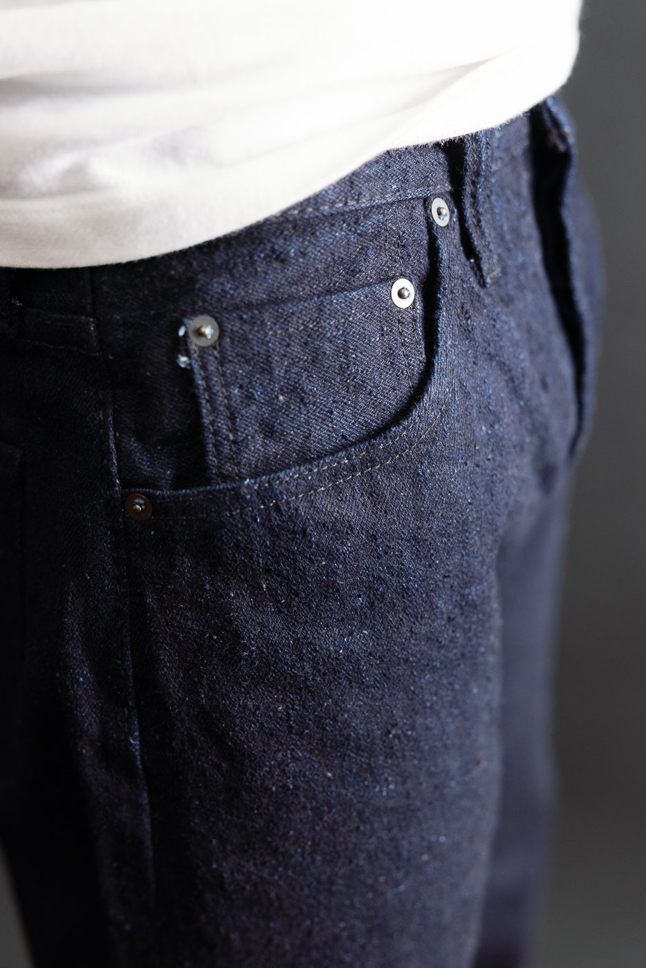 Close-up side view of dark indigo denim fabric texture and back pocket detail.