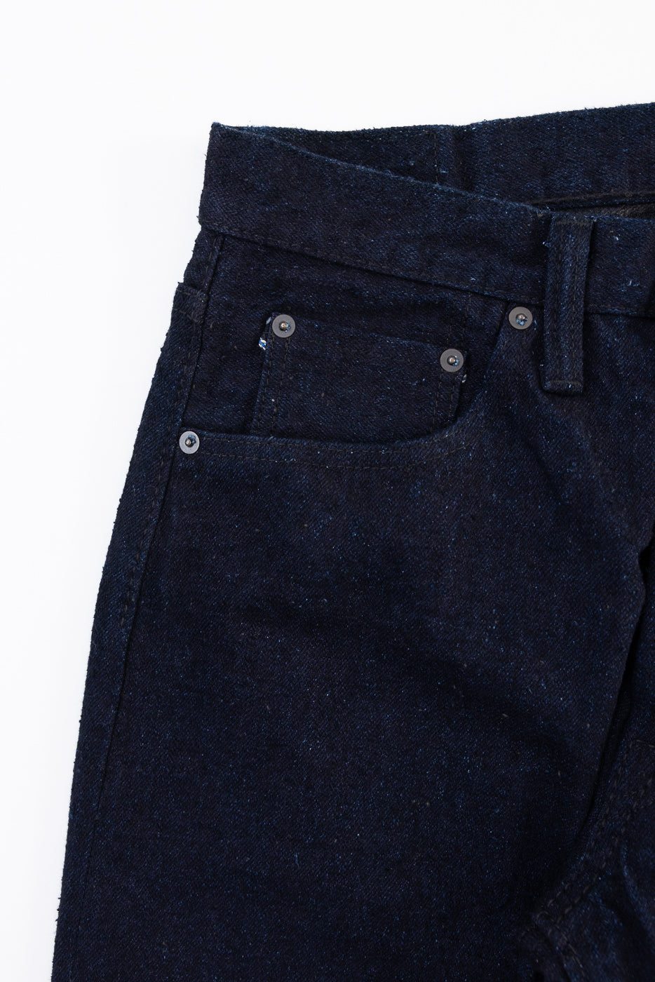 Close-up front view of dark indigo denim fabric texture and right front pocket detail.