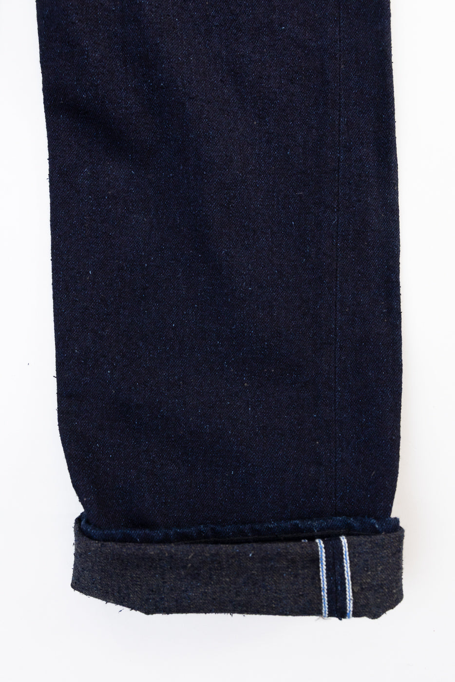 Close-up of the bottom hem of dark blue selvedge denim jeans, showing a cuffed leg.