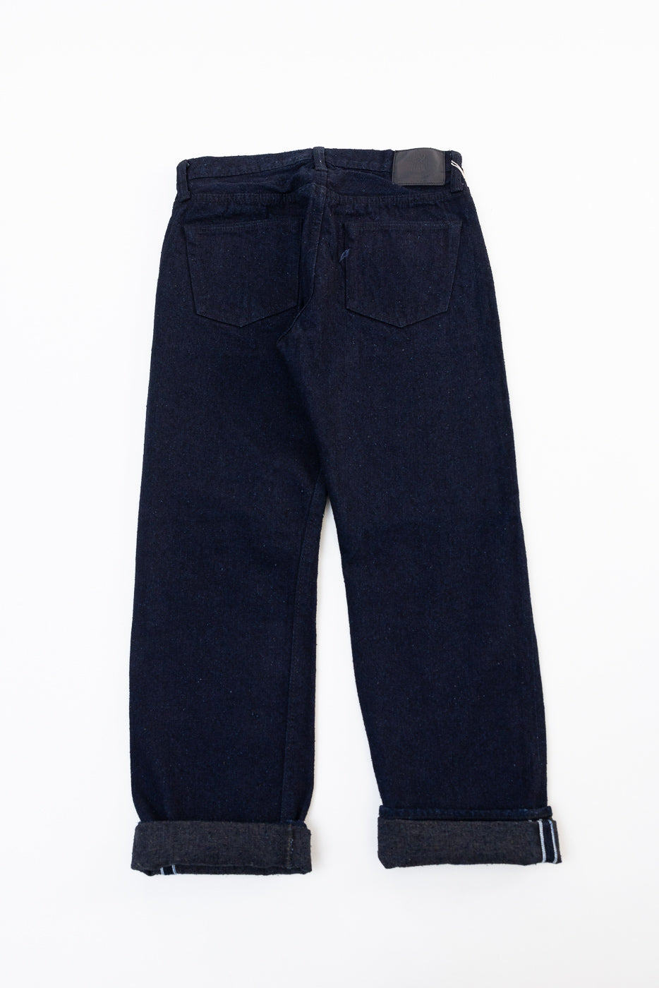 Back view flat lay of dark indigo selvedge denim jeans with cuffed hems.