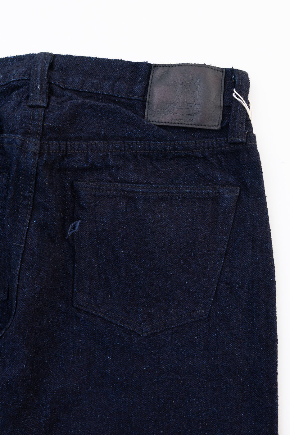 Close-up, back view of dark indigo denim jeans showing the rear pocket and leather waist patch.