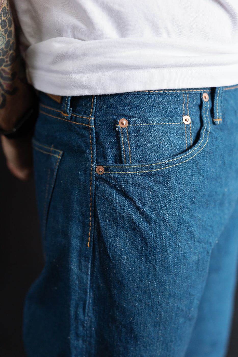 Close-up of front right hip and pocket of Pure Blue Japan greencast indigo selvedge jeans on male model, showing rivet details and fabric texture.