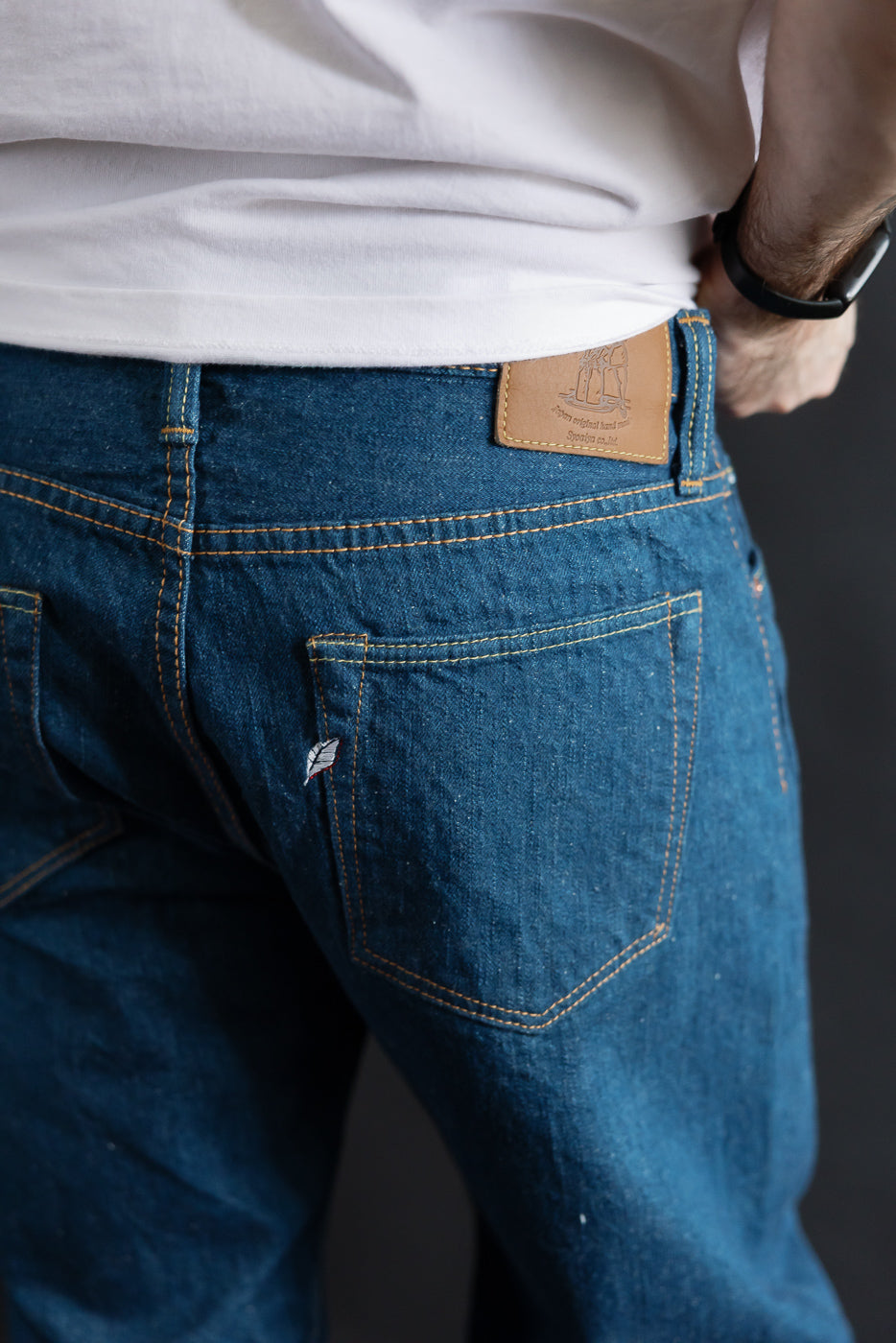 Close-up of back side Pure Blue Japan GRE-003 14oz greencast selvedge jeans on male model, showing leather patch and rear pocket details. Model is 5'9