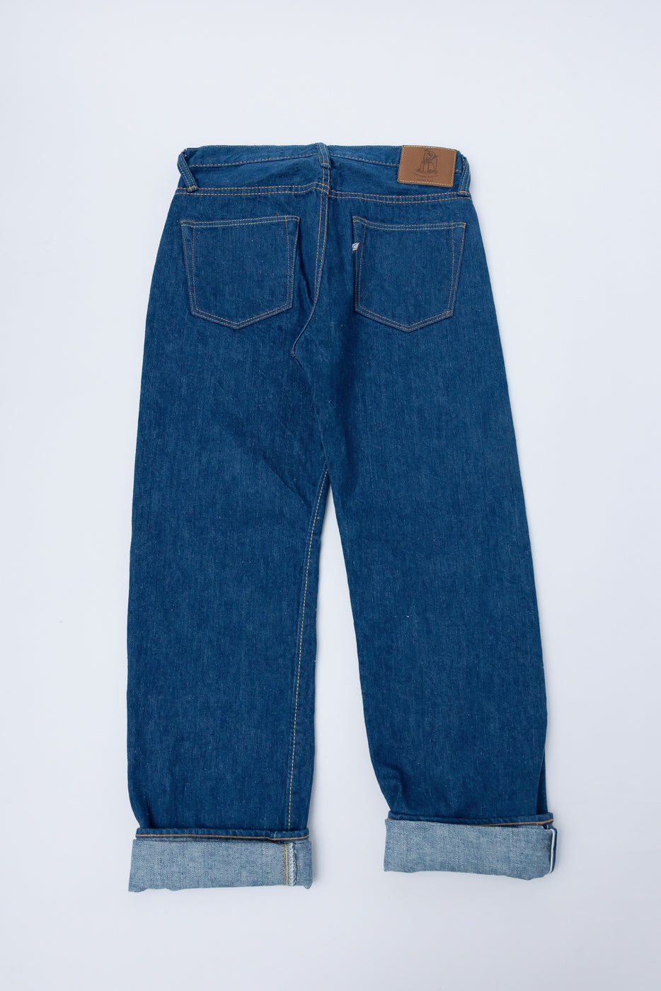 Back view flat lay of Pure Blue Japan GRE-003 14oz greencast indigo selvedge jeans with cuffed hems, showing rear pocket details and leather patch. Contemporary casual denim from Dant.