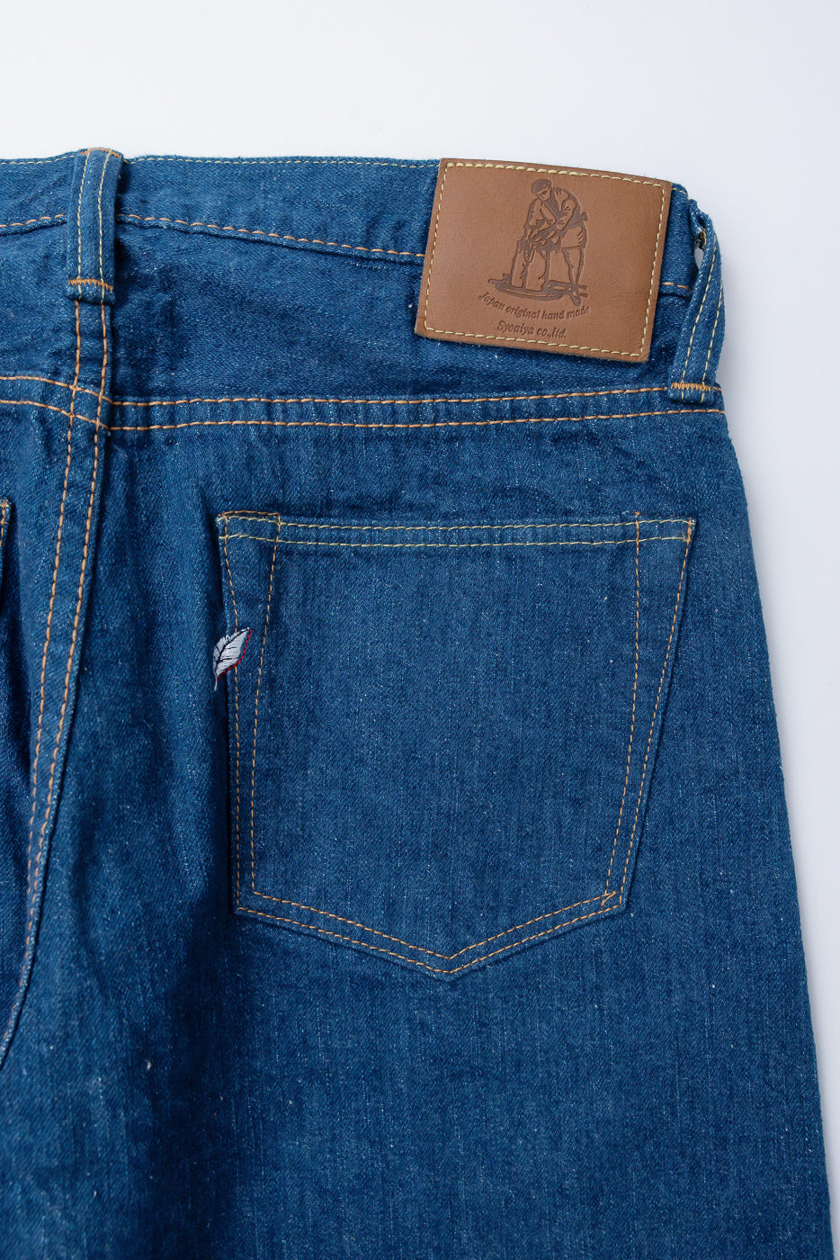 Close-up of back side Pure Blue Japan GRE-003 14oz greencast indigo selvedge jeans showing rear pocket, leather patch, and denim texture.