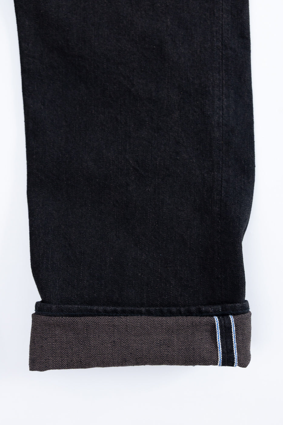 Close-up of black selvedge jeans hem, showing rolled cuff with blue and white selvedge stripe detail