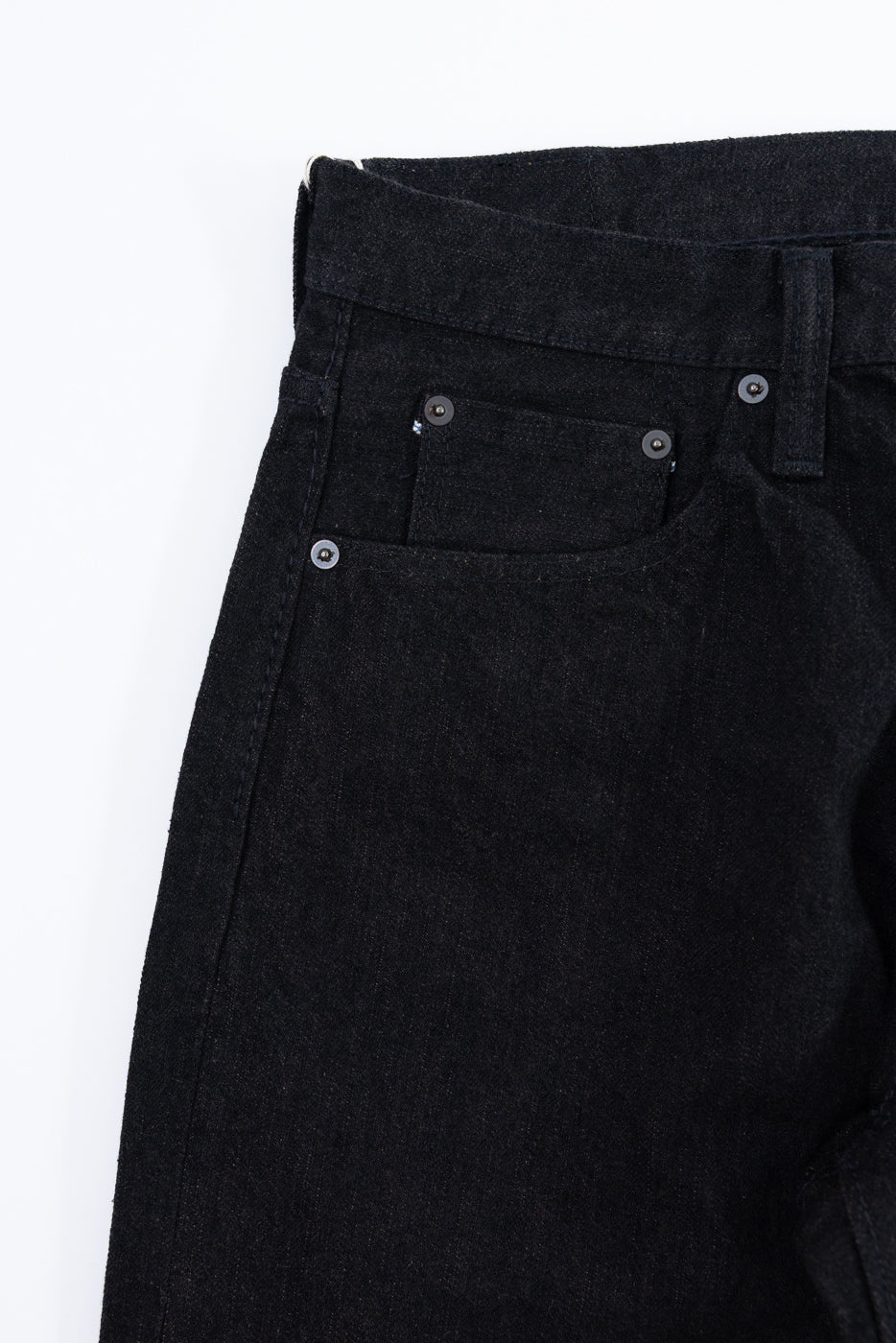 Close-up front view of dark selvedge denim jeans showing button fly, front pocket, and waistband details