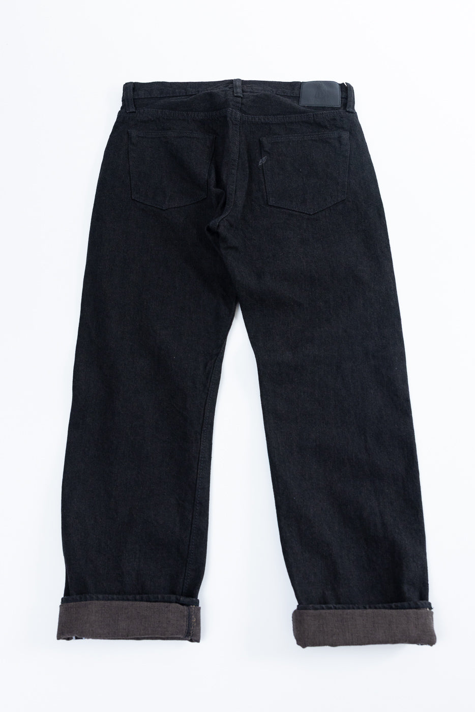 Back view flat lay of dark selvedge jeans, cuffed hems, two back pockets, leather patch waistband