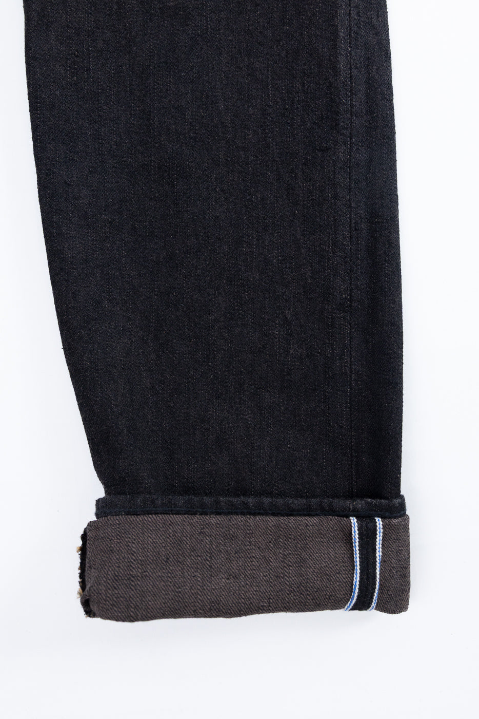 Close-up of dark selvedge denim jeans leg, showing rolled cuff with blue and white stripe detail.