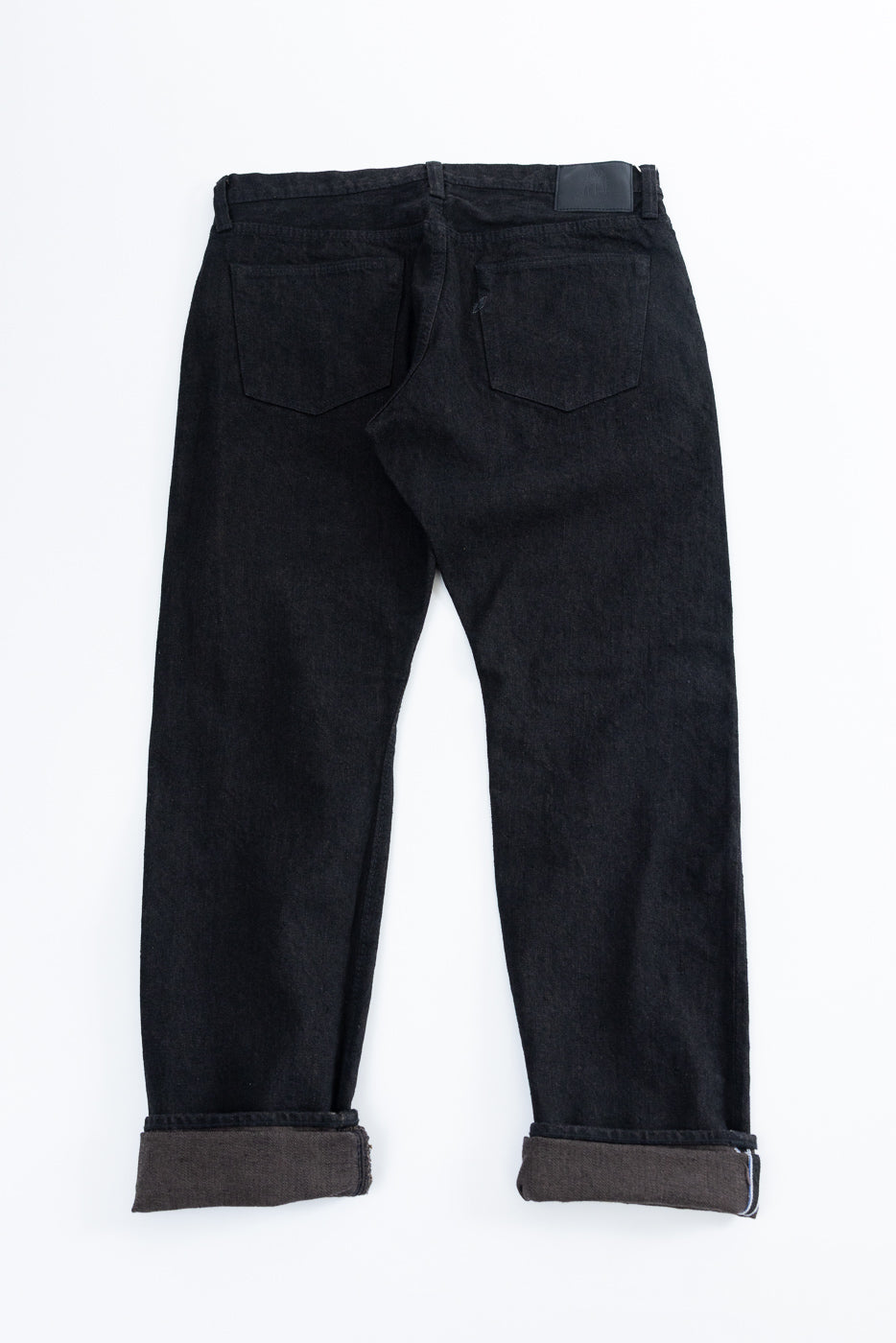 Back view of black selvedge jeans, cuffed hem showing contrast lining, flat lay