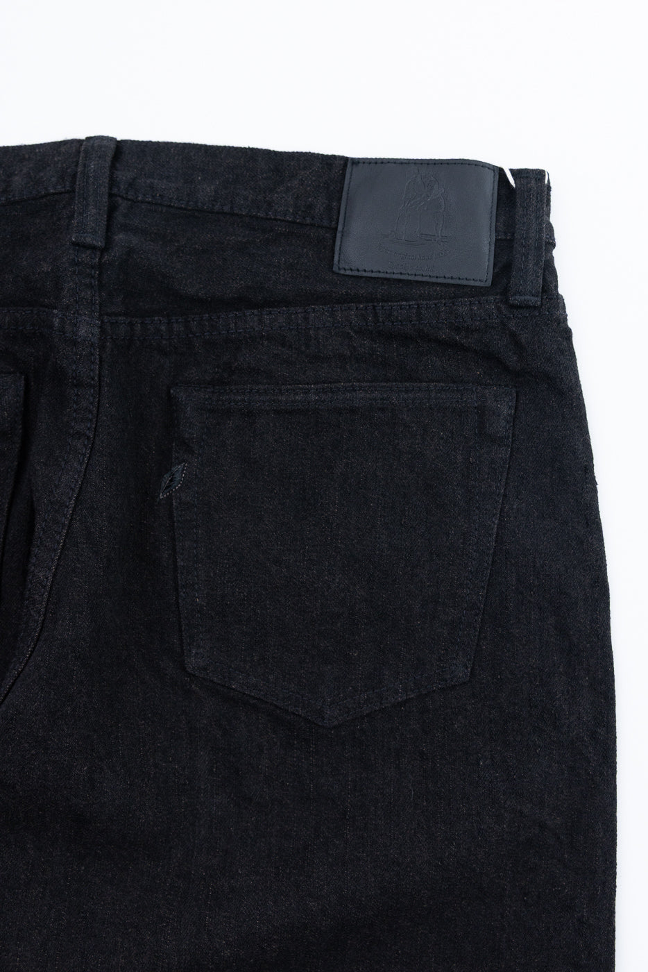 Back view of dark selvedge jeans, close-up on rear pocket and leather patch detail
