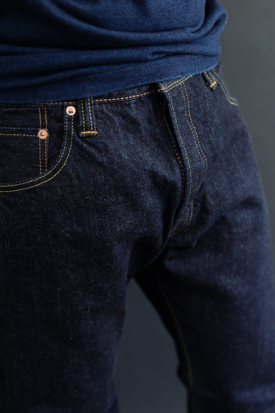 Close-up front view of dark selvedge denim jeans with yellow stitching, worn by male model, 5'9