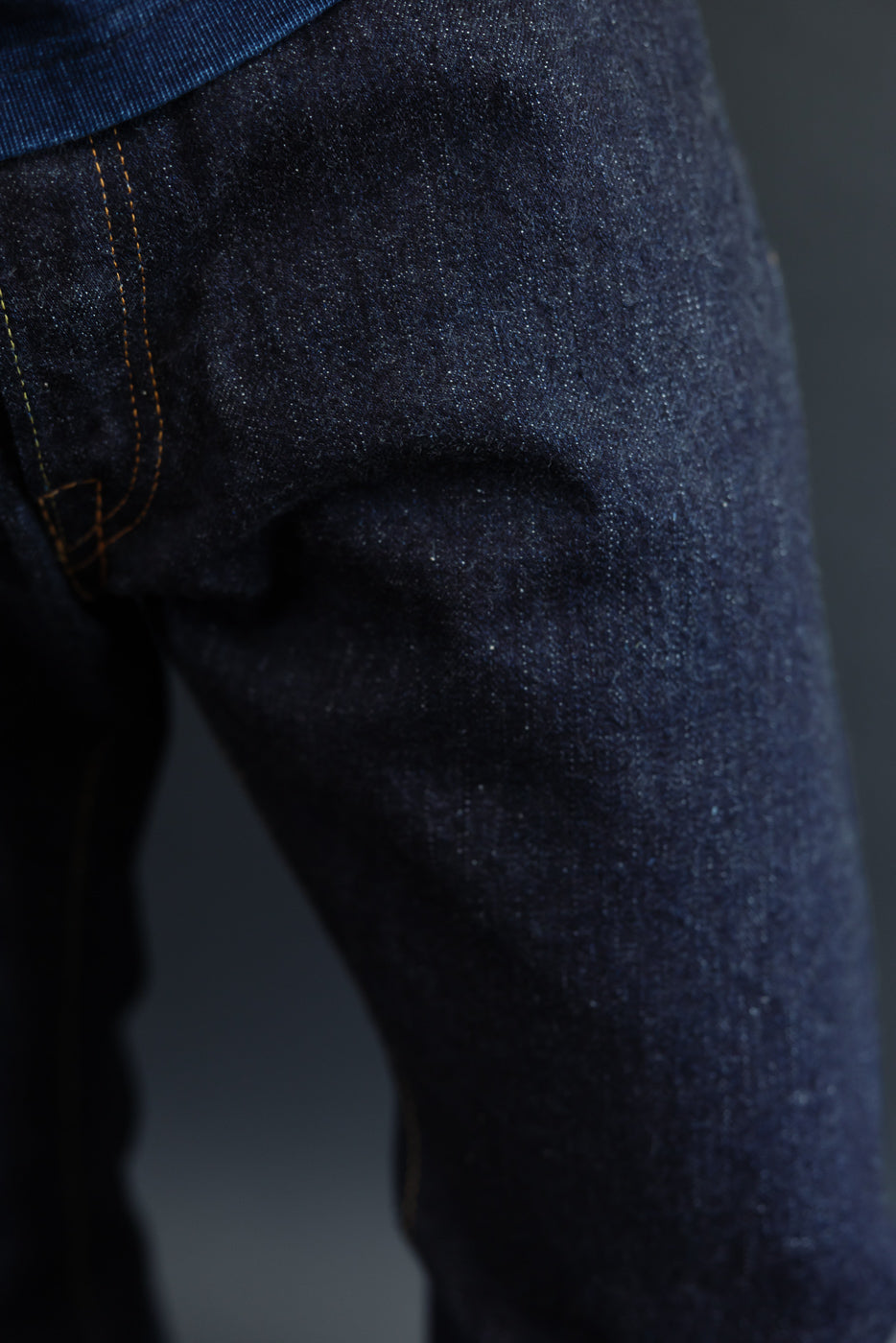 Close-up of dark selvedge denim jeans, showcasing texture and orange stitching on male model's thigh.