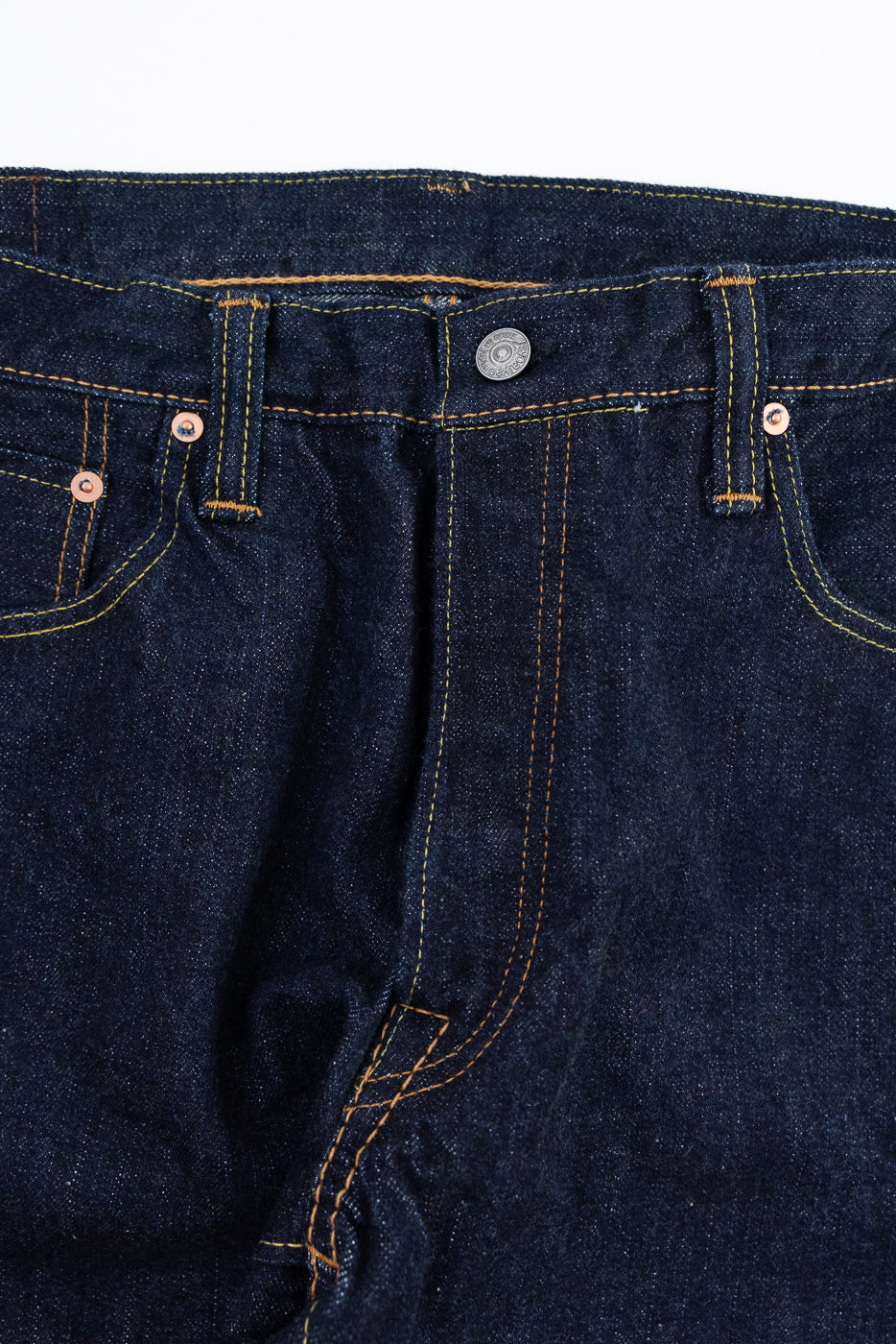 Close-up front view of dark selvedge denim jeans with yellow stitching, button, and copper rivets