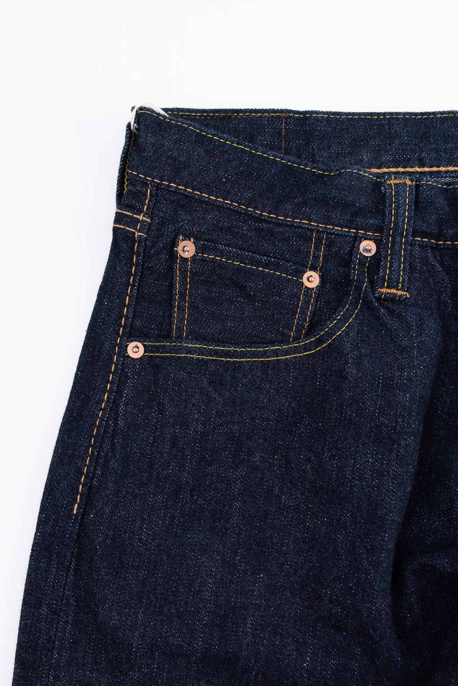 Close-up front view of dark selvedge denim jeans with copper rivets and yellow stitching