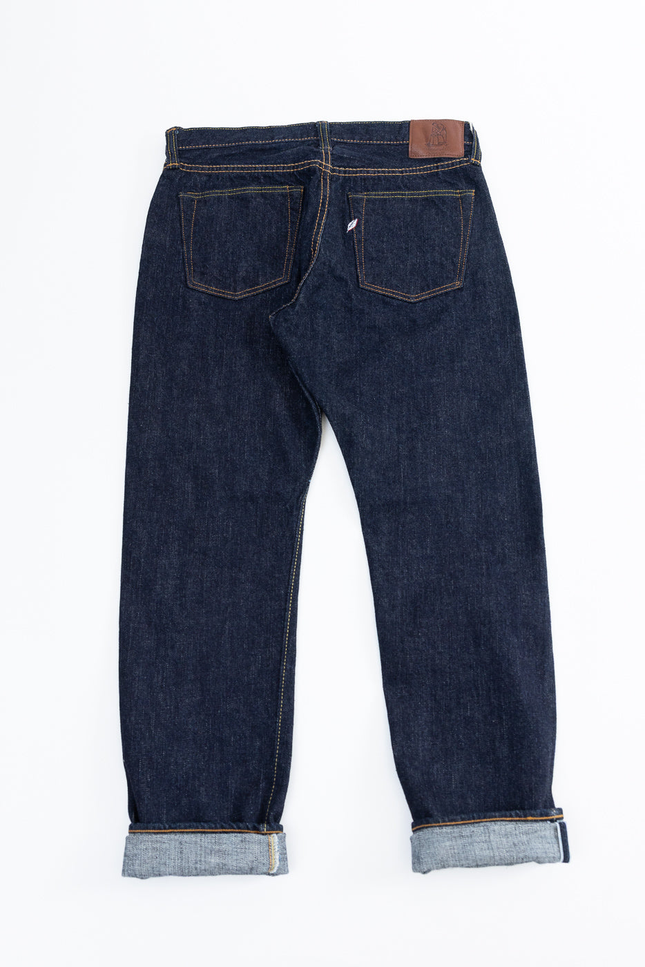 Back view of selvedge denim jeans with cuffed hems, brown leather patch, and contrast stitching