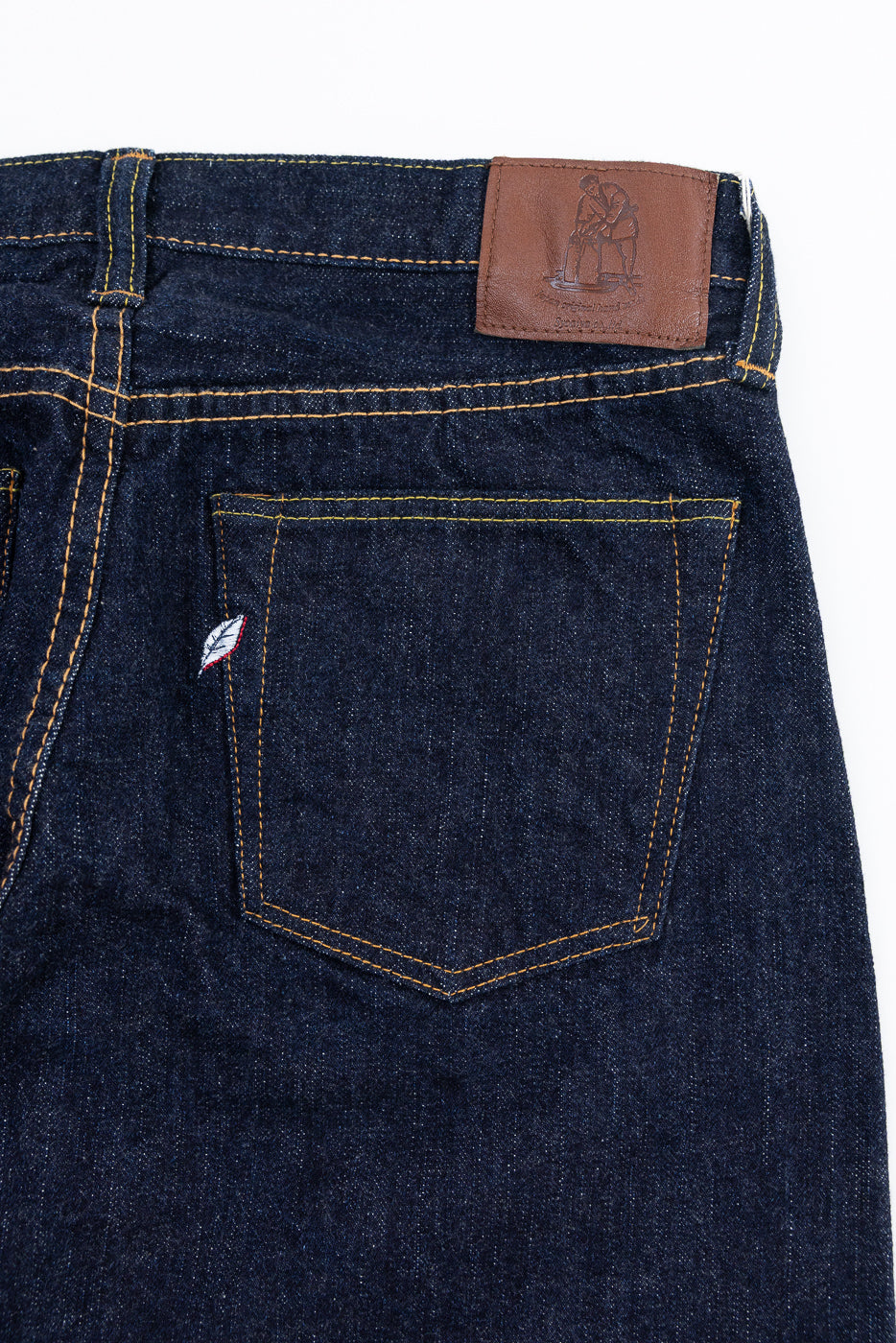 Close-up back view of dark selvedge denim jeans showing leather patch, back pocket, and contrast stitching
