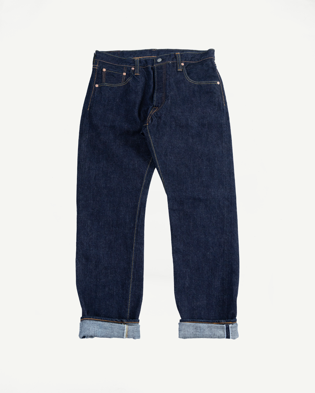 Front view flat lay of dark selvedge denim jeans with cuffed hems, copper rivets, and contrast stitching