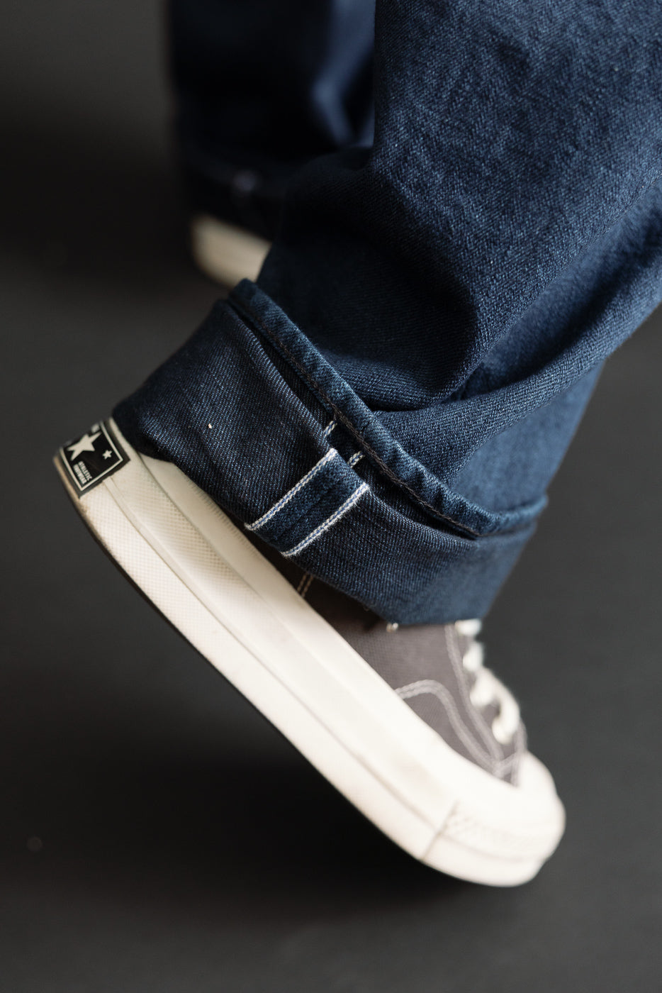 Close-up of the hem of dark blue selvedge denim jeans worn by a male model.