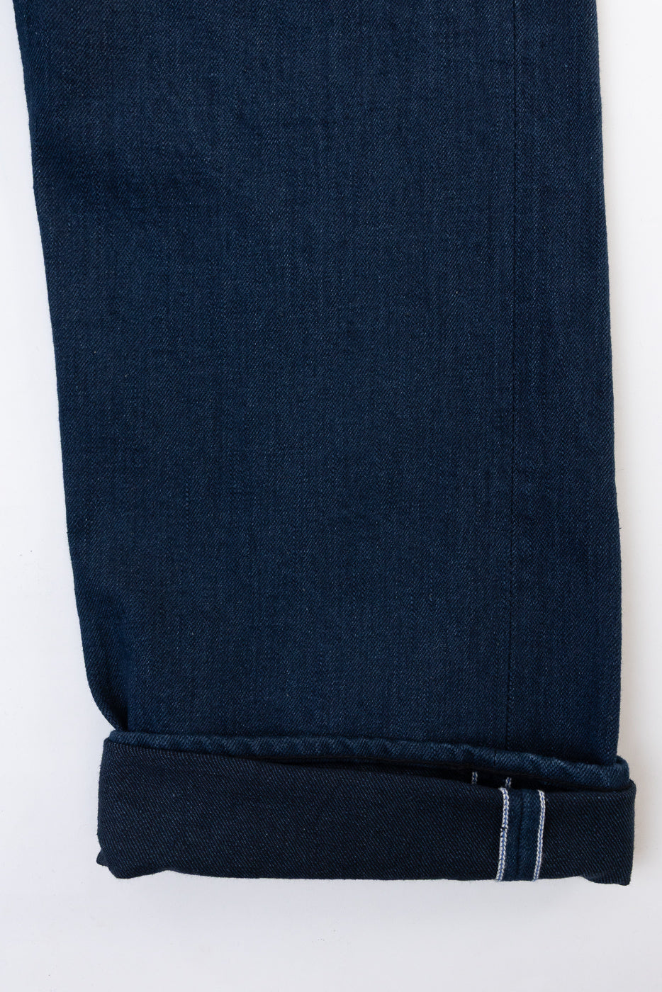 Close-up of the hem and selvedge detail on the bottom of dark indigo denim jeans.