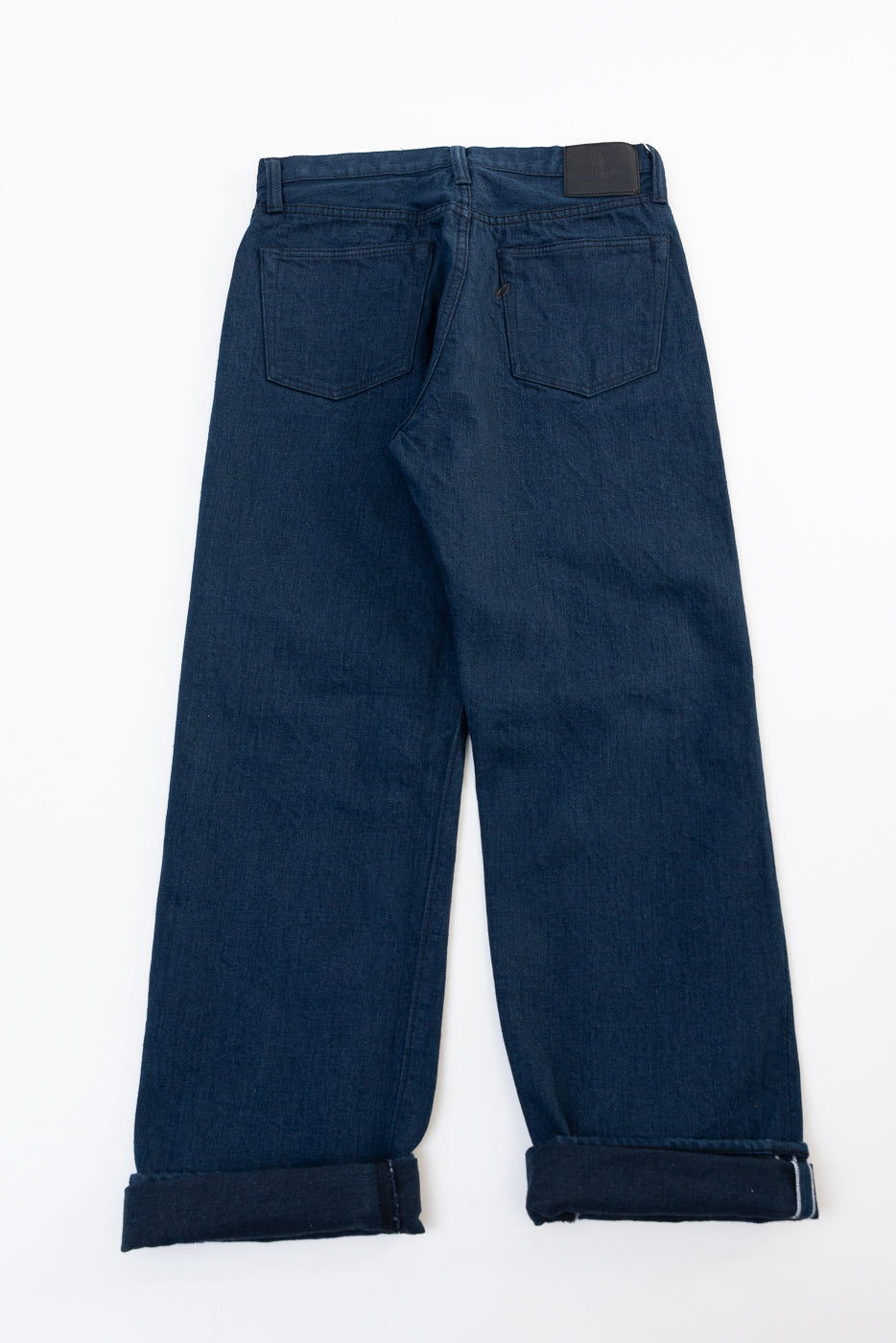 Back view flat lay of dark wash selvedge denim jeans with cuffed hems.