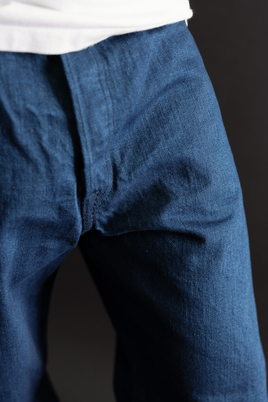 Close-up of the front crotch and fly area of blue denim trousers showing fabric texture.