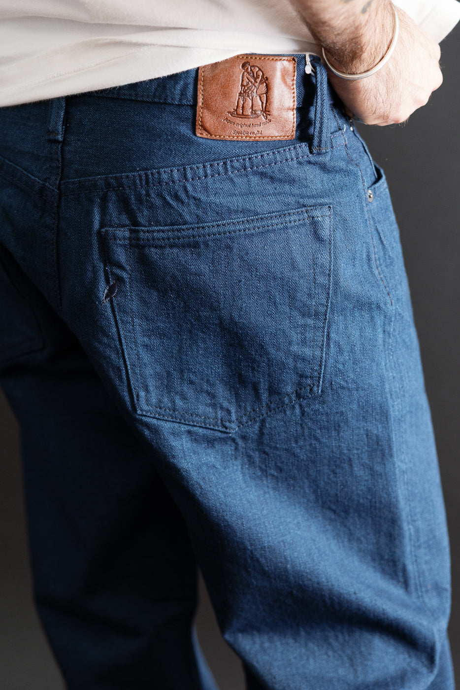 Close-up back view of blue denim jeans showing the leather patch and rear pocket detail.