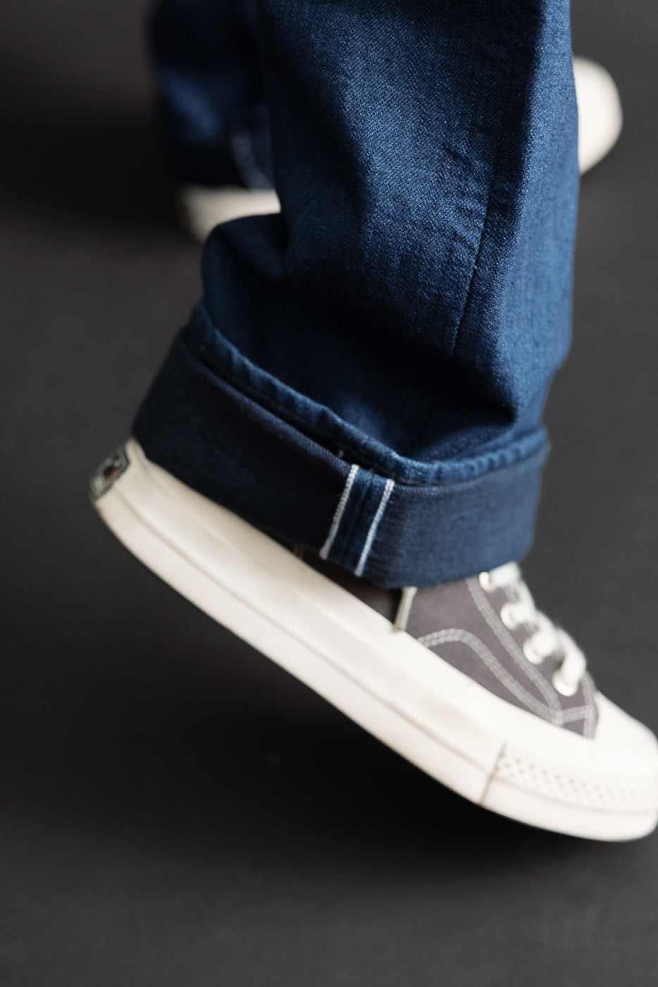 Close-up of the bottom hem and cuff of blue denim jeans paired with dark canvas sneakers.