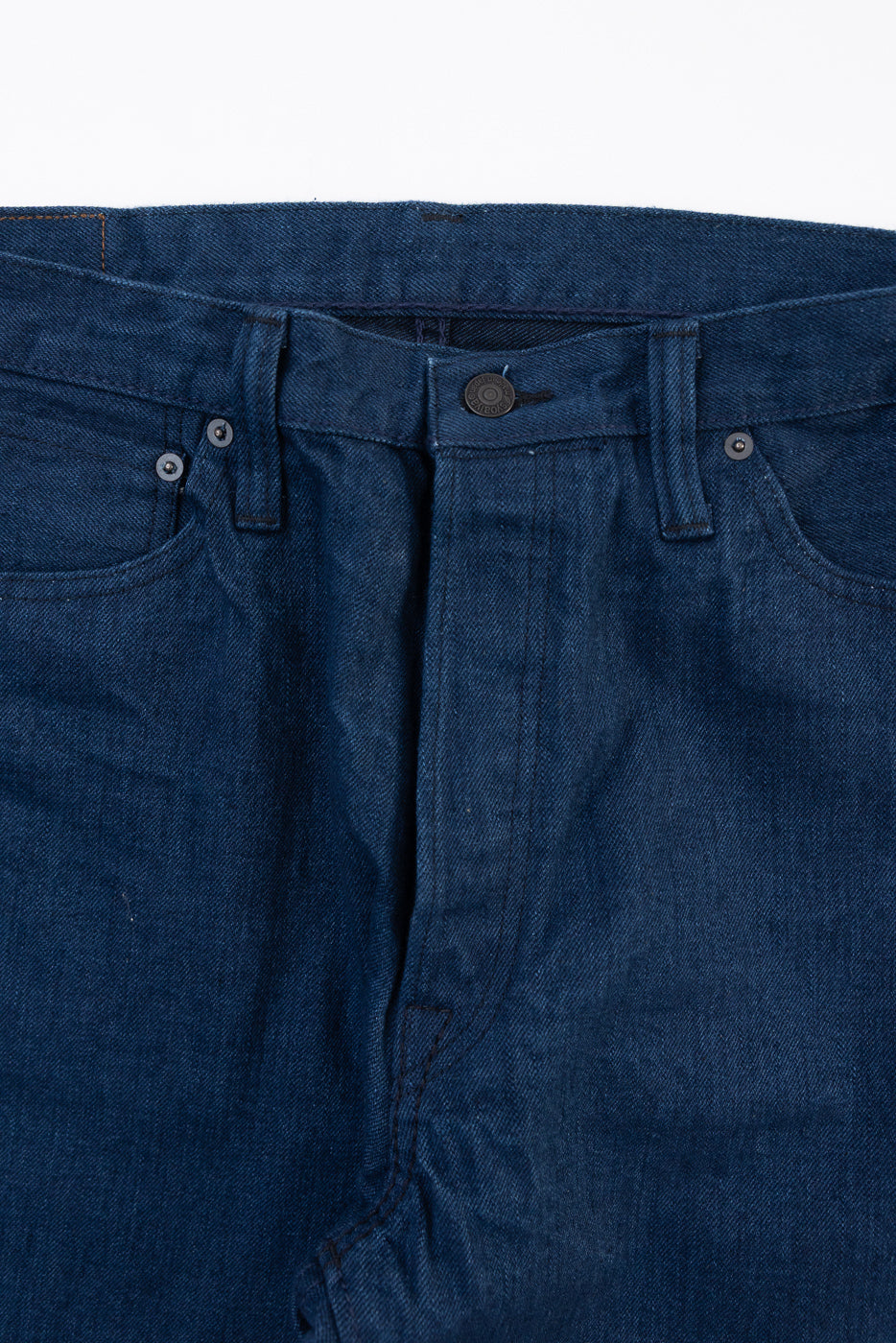 Close-up front view of dark indigo selvedge denim jeans showing waistband and button fly.