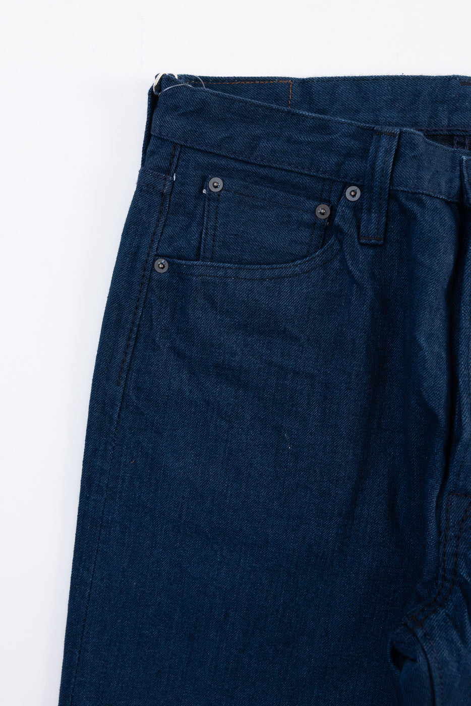 Close-up of the front right hip of dark indigo selvedge denim jeans showing pocket and rivets.