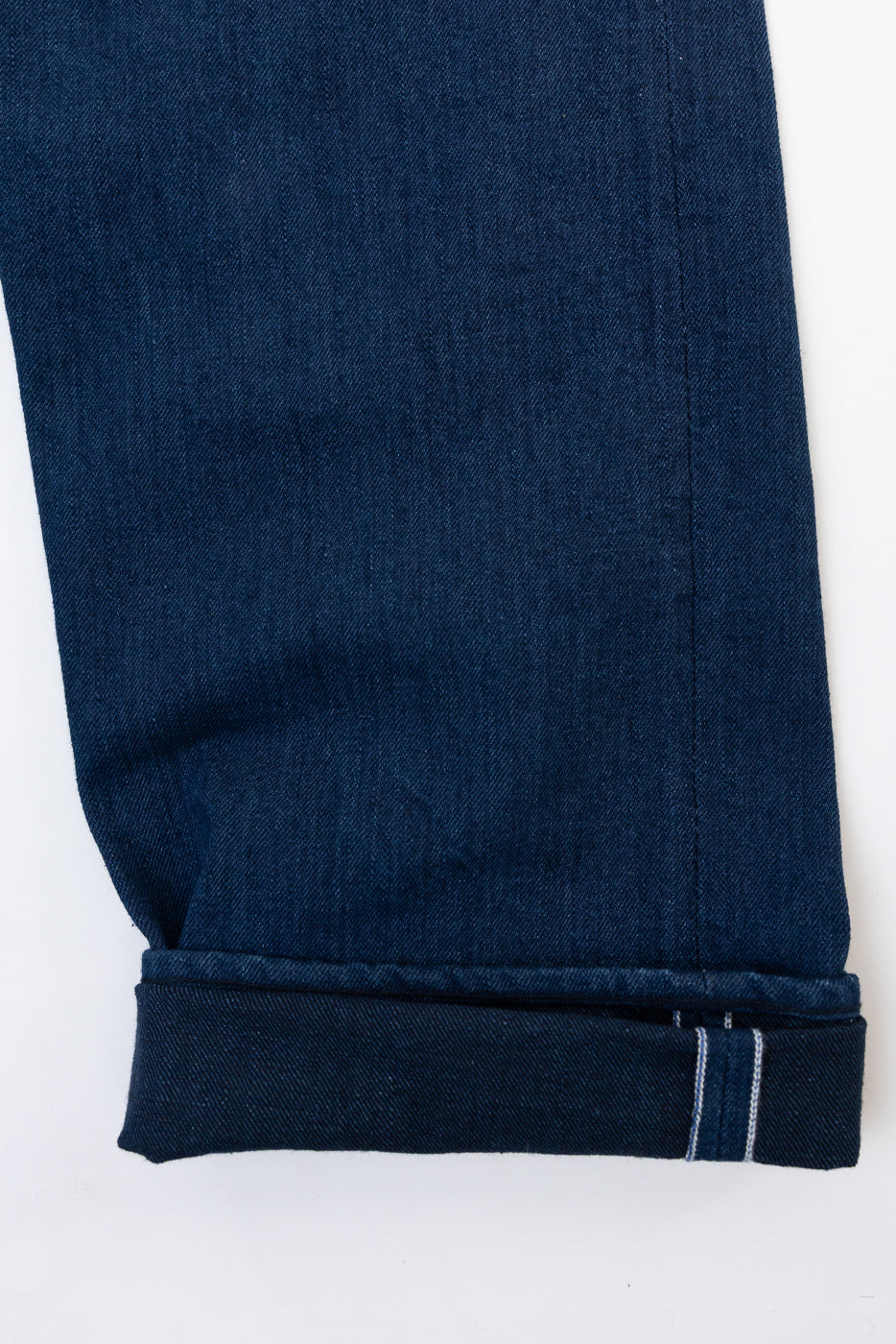 Close-up of the bottom hem and cuff of dark indigo denim jeans, showing the white selvedge detail.