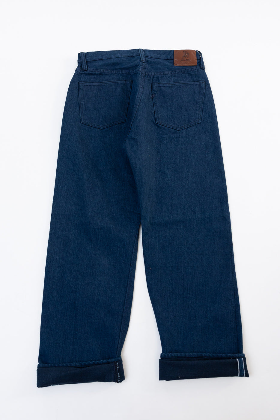 Back view flat lay of dark indigo denim jeans with cuffed hems.