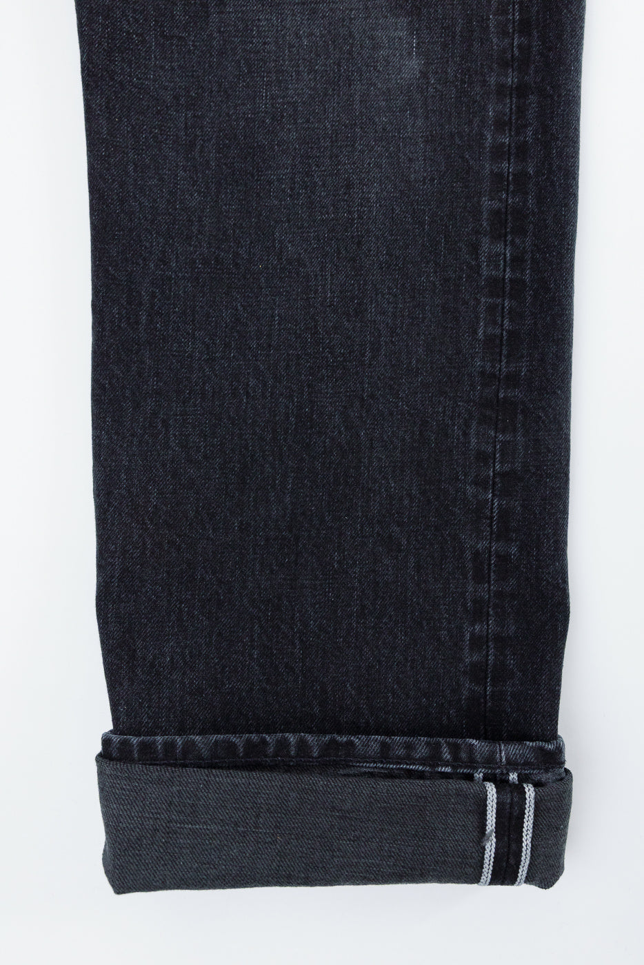 Close-up of dark selvedge denim jeans leg, front view, showcasing hem and white stitching detail.
