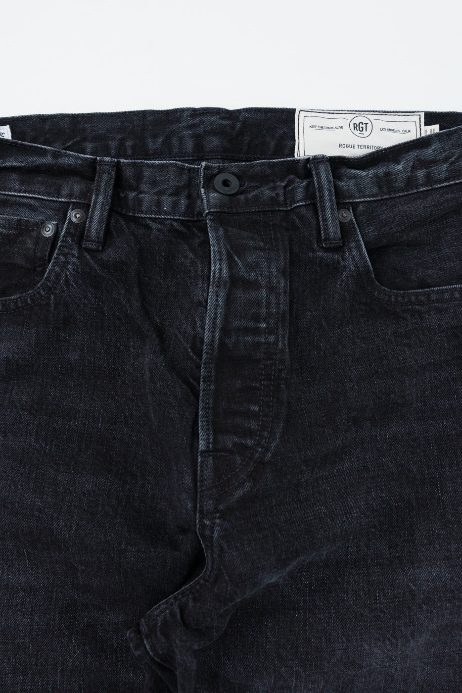 Close-up front view of dark selvedge denim jeans showing waistband, button fly, and RGT brand tag detail