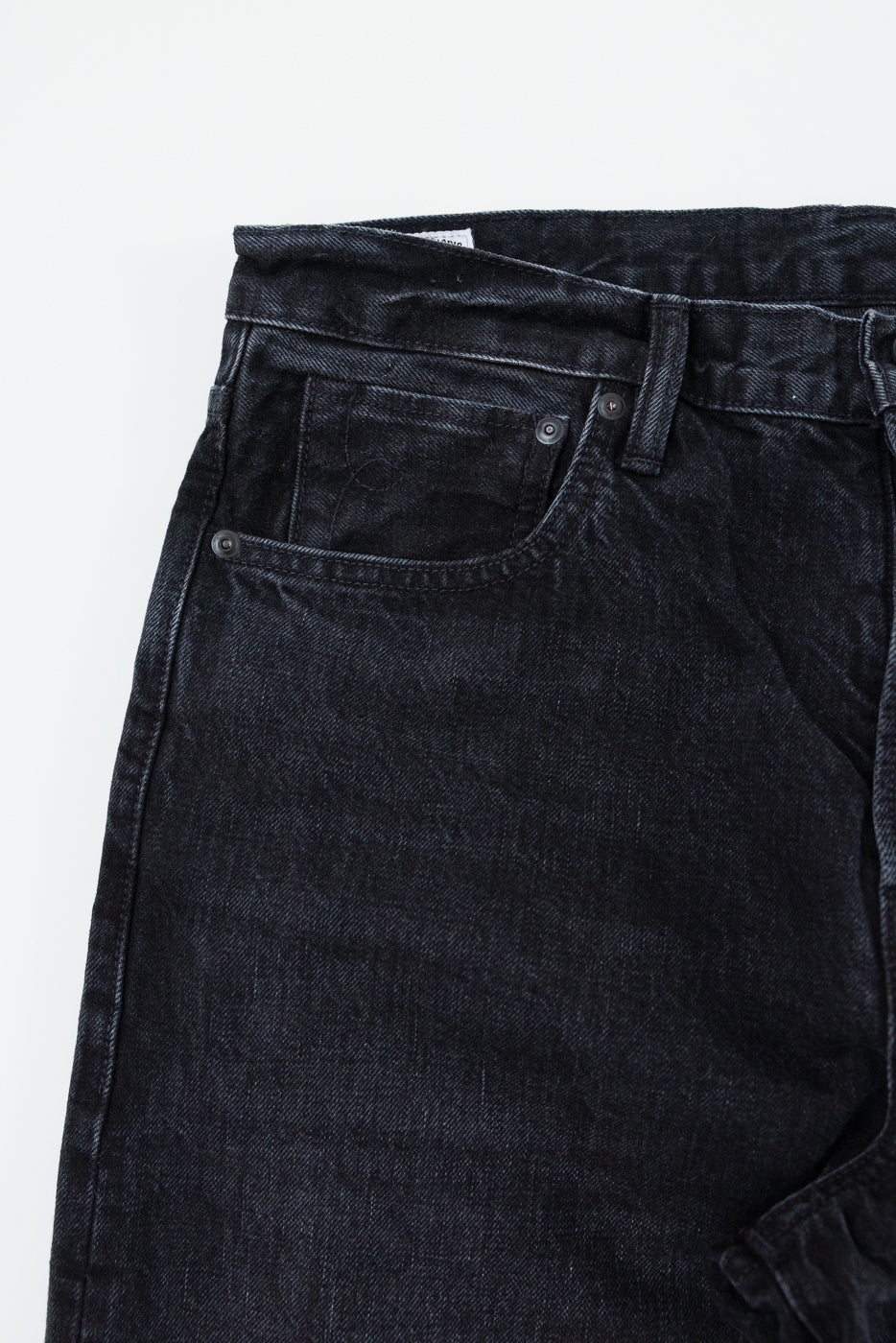 Close-up front view of dark selvedge denim jeans, showcasing texture, button, and pocket details.