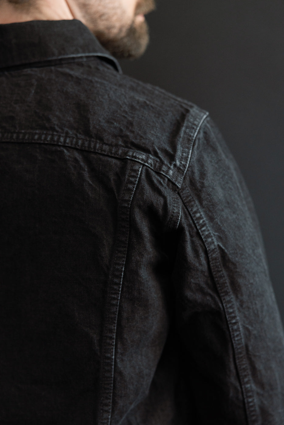 Close-up of back shoulder and seam details on black denim jacket, male model, athletic build