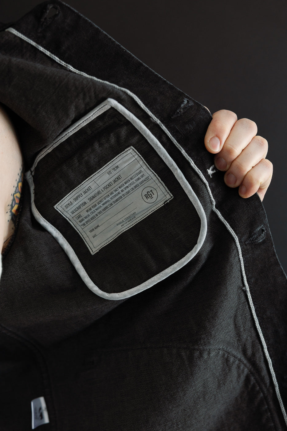 Close-up of inside front left panel of men's supply jacket, showing interior label and seam details.