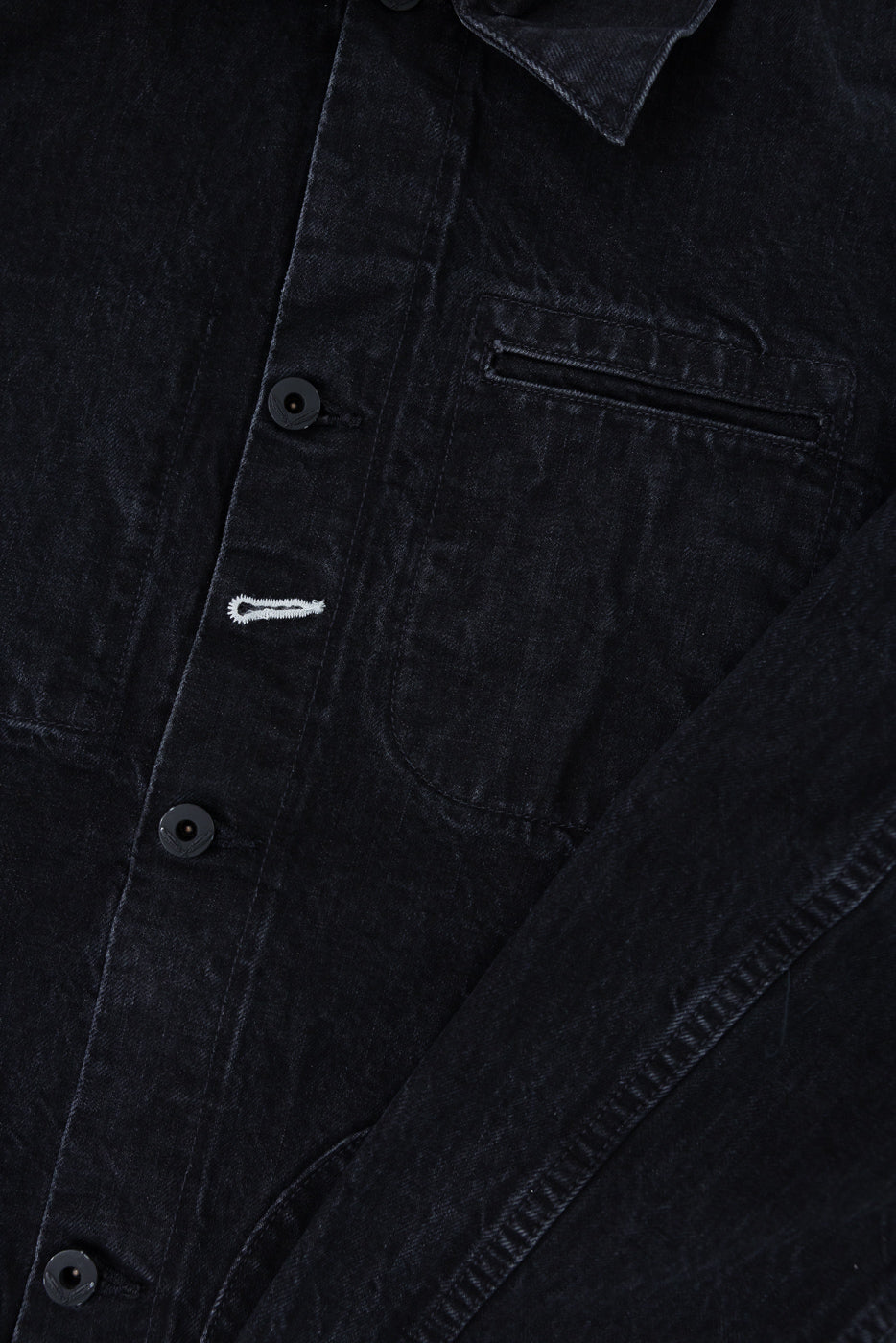 Close-up of front chest area on black denim jacket, buttons, pocket, collar, fabric texture visible.