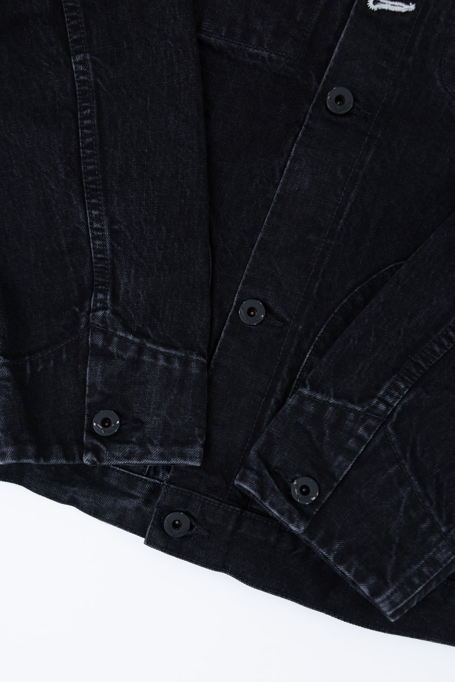 Close-up of front hem and button details on black denim jacket, showing fabric texture