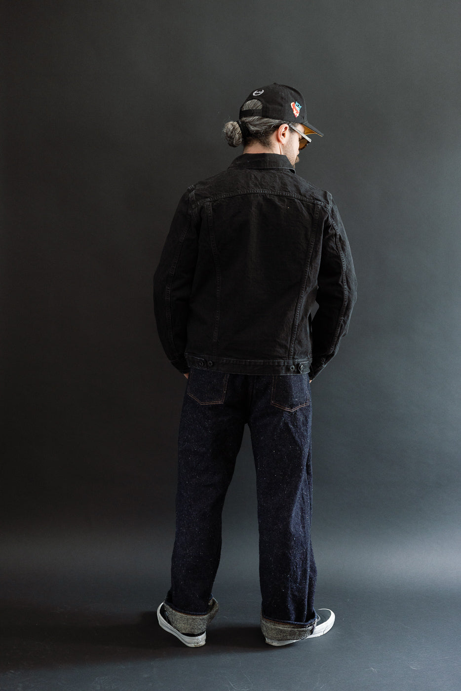 Full body rear view of male model 5'9, 165lbs athletic build wearing black denim jacket and dark jeans